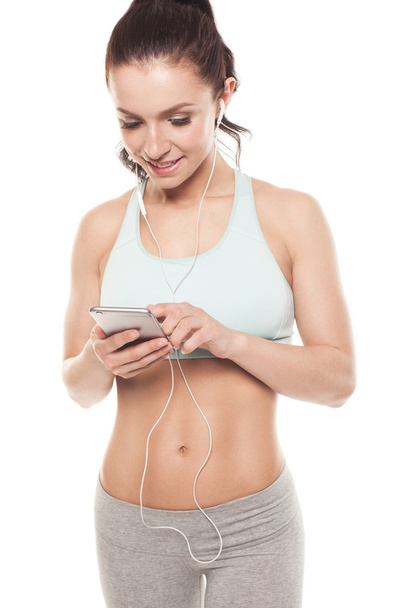 fitness girl with a smartphone on a white background, enjoys sports training, gym workout - Photo, image