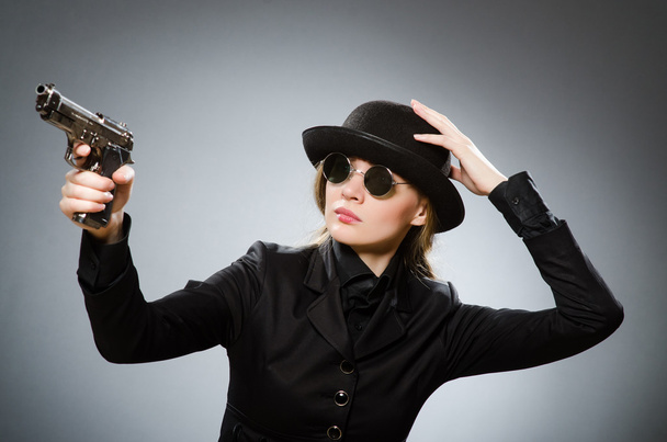 Female spy with weapon against gray - 写真・画像