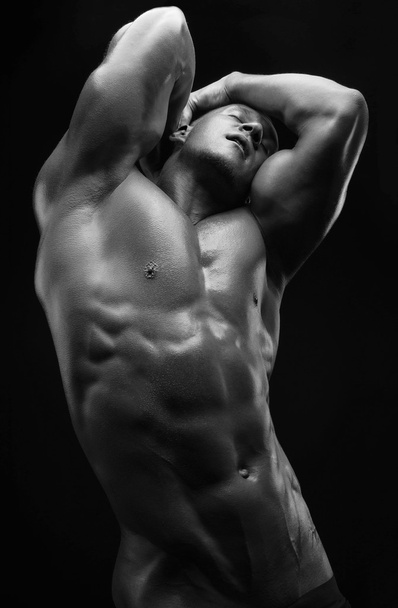 Bodybuilder and strip theme: beautiful with pumped muscles naked man posing in the studio on a dark background, black-and-white photo - Fotografie, Obrázek