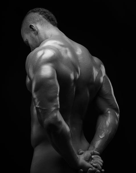Bodybuilder and strip theme: beautiful with pumped muscles naked man posing in the studio on a dark background, black-and-white photo - Fotó, kép