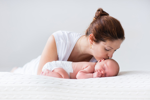Jonge moeder en pasgeboren baby in witte slaapkamer - Foto, afbeelding