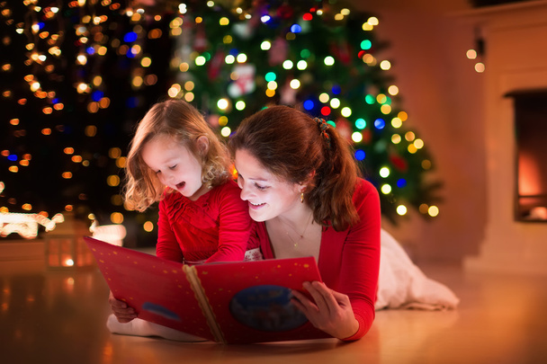 Mãe e filha lendo no lugar do fogo na véspera de Natal
 - Foto, Imagem