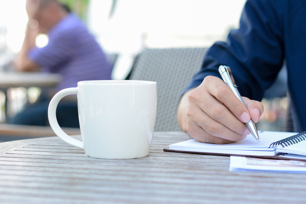 ein Mann schreibt auf Notizbuch mit Kaffeetasse daneben - Foto, Bild