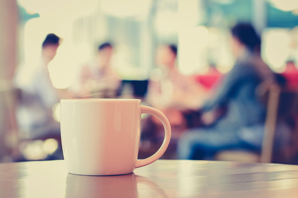 Šálek kávy na stole s lidmi v kavárně jako rozostření pozadí - Fotografie, Obrázek