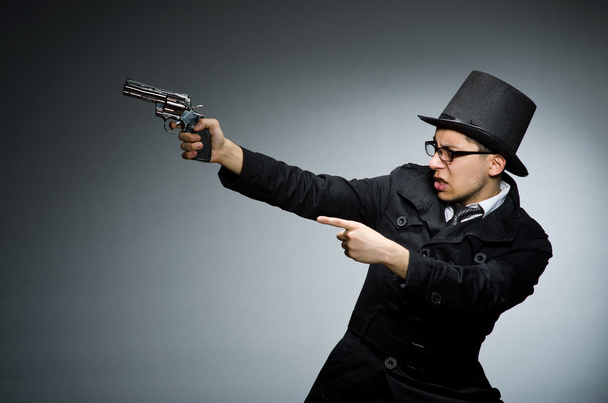 Zločinec v černém kabátě, drží hadgun proti šedi - Fotografie, Obrázek