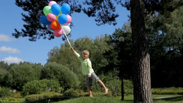 boldog fiú állandó léggömbökkel a zöld park - Felvétel, videó