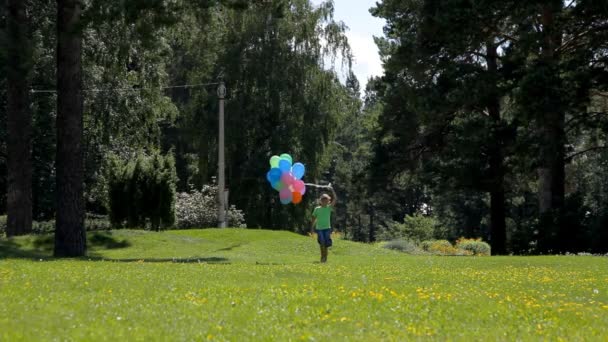happy boy with balloons walking in green park - Záběry, video