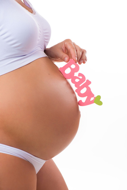 Pink label "Baby" a kezében terhes nő. Az újszülött lánya. Terhes hasa közelről, fehér alapon. - Fotó, kép