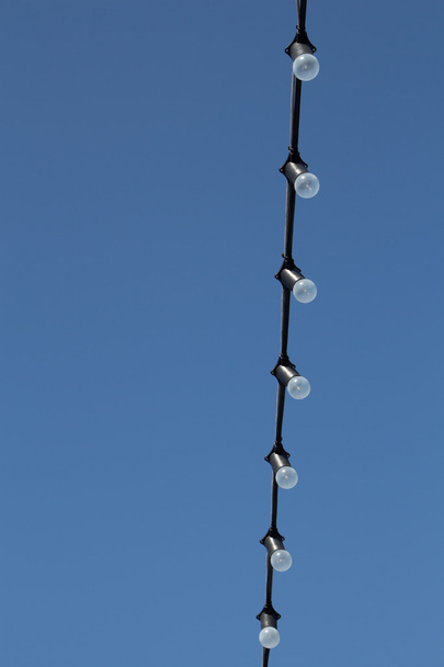 Cordão com uma fileira de lâmpadas em contra o céu azul
 - Foto, Imagem