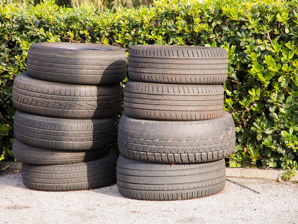 Montón de neumáticos desgastados usados arbustos verdes en el fondo
 - Foto, Imagen