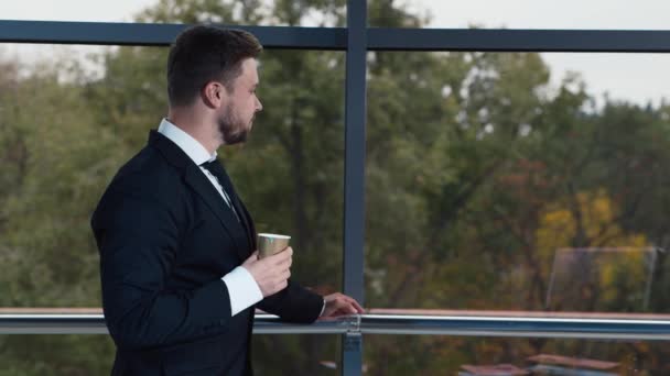 Young businessman drinking coffee at office window - Footage, Video