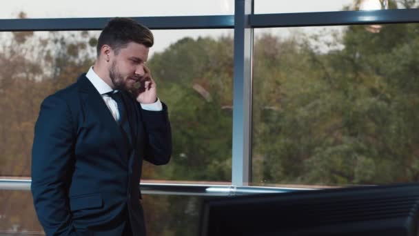 Young businessman talking on the phone at the office window - Materiał filmowy, wideo