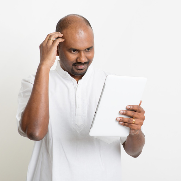 Mature casual business Indian man using tablet pc and scratching - Foto, imagen