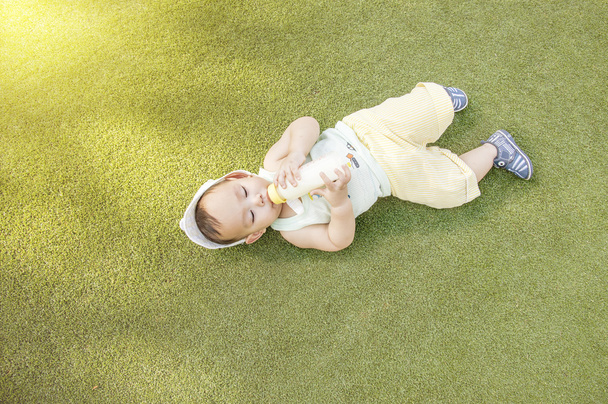 Asian baby drinking milk from bottle while he's laying on the gr - Photo, image