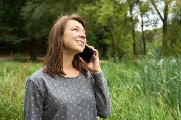onnellinen nuori nainen puhuu puhelimessa metsässä
 - Valokuva, kuva