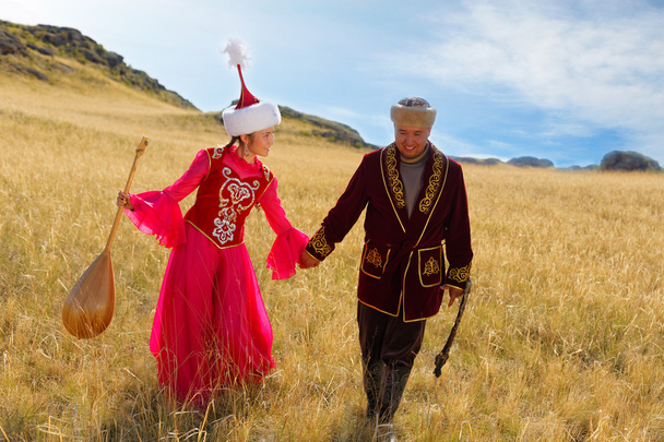 Kazajstán hombre y mujer en trajes nacionales en la estepa jugando dombyra y bailando
 - Foto, imagen