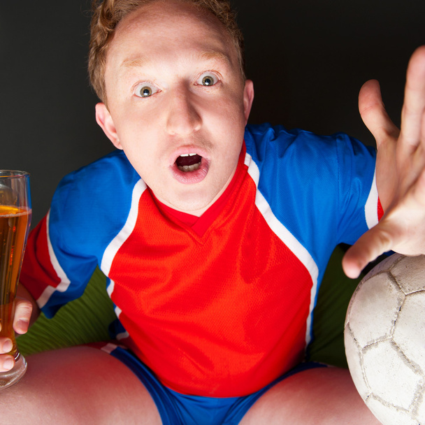 Young man holding soccer ball and beer and watching tv translati - Foto, Imagen