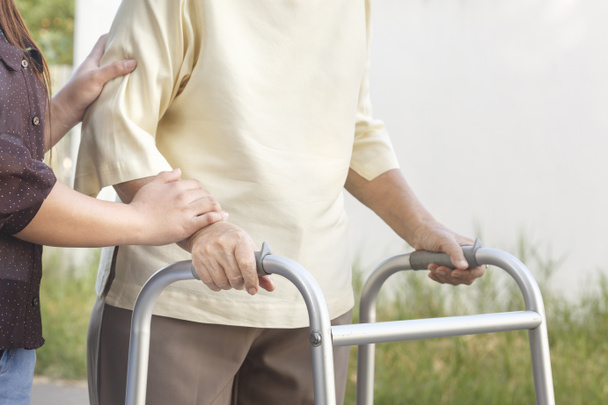 vanhempi nainen, joka käyttää kävelijää hoitajan kanssa
 - Valokuva, kuva