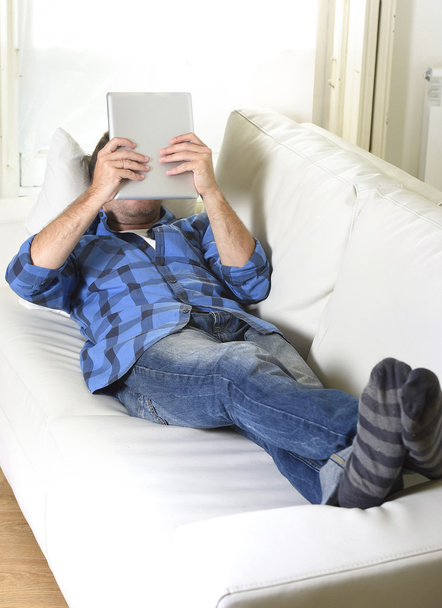 jeune homme attrayant des années 30 en utilisant tablette numérique couché sur le canapé à la maison réseau regardant détendu
 - Photo, image