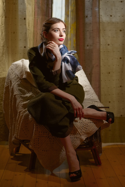 Lady in dark room sitting in armchair in wool dress and silk scarf - Fotó, kép