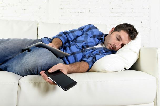 привлекательный мужчина спит на домашнем диване с мобильным телефоном и цифровым планшетом в руках
 - Фото, изображение