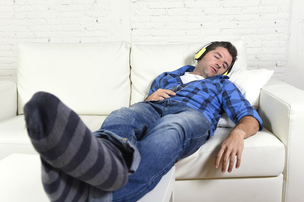 Mann schläft auf der heimischen Couch ein, während er mit Handy und Kopfhörer Musik hört - Foto, Bild