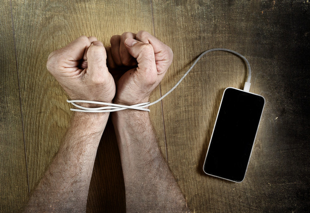 man hands wrapped on wrists with mobile phone cable handcuffed in smart phone networking addiction concept - Fotografie, Obrázek