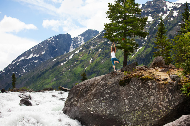Young woman is practicing yoga at mountain river - Photo, Image