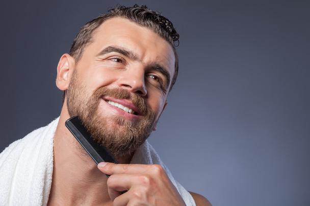 Cheerful young bearded guy with comb and smile - Photo, Image