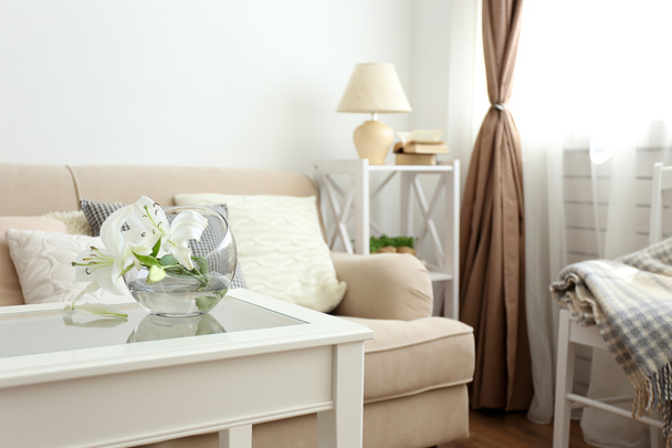 Pastel color sofa with beautiful pillows and vase with flowers on the table in front of it in the room - Valokuva, kuva