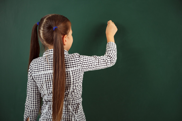 Beautiful little girl writing on blackboard - Фото, изображение