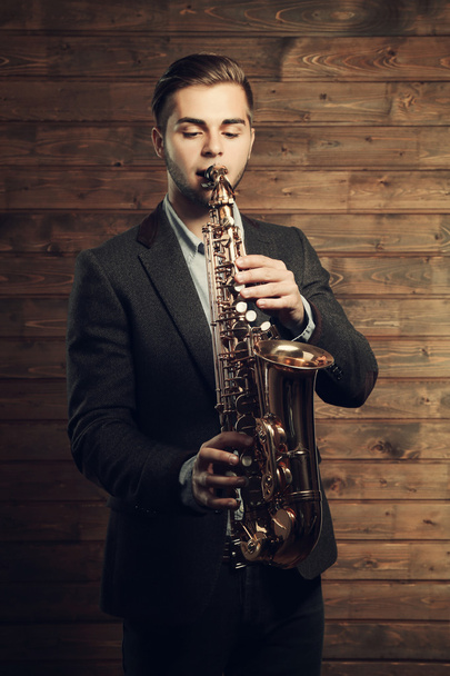 Elegant saxophonist plays jazz on wooden background - Foto, Imagen