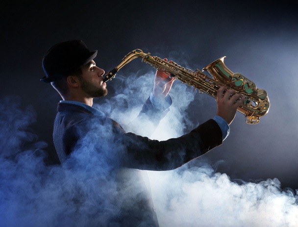 Elegant saxophonist plays jazz on dark background in a smoke - Foto, afbeelding