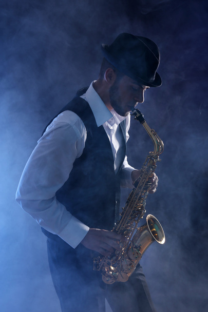 Elegant saxophonist plays jazz on dark background in blue smoke - Foto, imagen