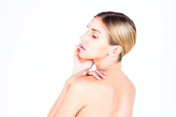 Young woman with beautiful skin and a naked back looking down and touching her face. Beauty concept. - Photo, Image