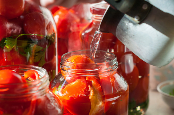 Processo de enlatamento de tomate em frasco de pedreiro. No fundo há poucos jarros com tomates. Conservação e cozimento
 - Foto, Imagem