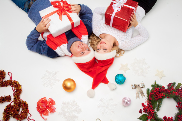 Preciosa pareja de Navidad en Santa Claus sombreros acostados con regalos sobre fondo blanco
 - Foto, imagen