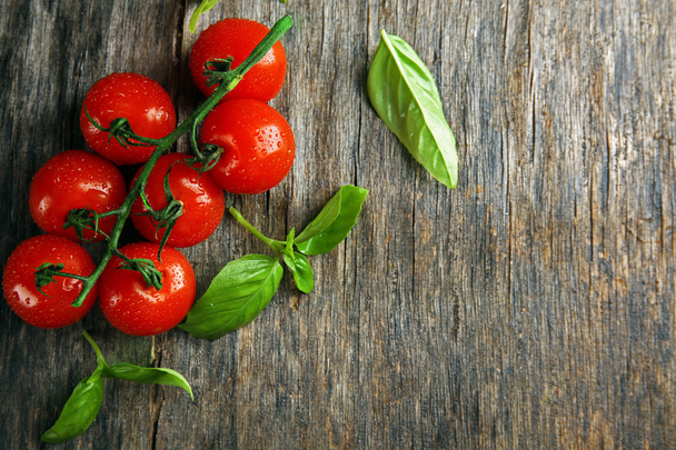 Cherry tomatoes with basil on wooden table close up - Foto, afbeelding