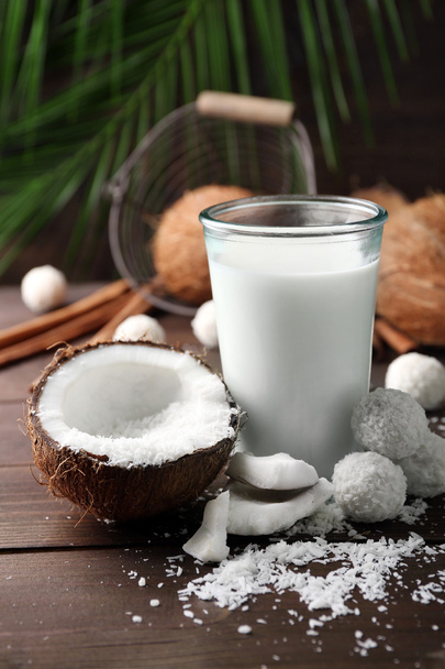 Candies in coconut flakes, glass of milk and fresh coconut on dark wooden background - Foto, Imagem