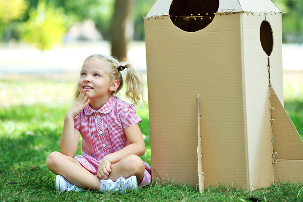 Little girl sitting near carton rocket - Foto, imagen