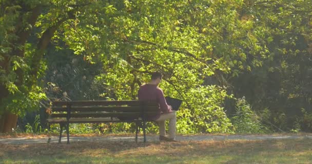 Man is Sitting on Bench Freelancer Copywriter Designer Programmer Accountant is Working with Laptop Has Closed the Laptop Put Backpack On Walks Away - Záběry, video