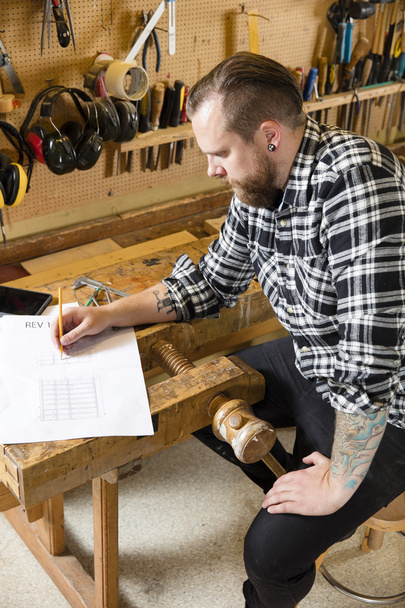 Carpinteiro planeja projetos e toma notas sobre desenho em oficina
 - Foto, Imagem