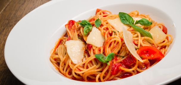 Espaguetis con tomate, parmesano y albahaca servidos en un plato blanco
 - Foto, imagen