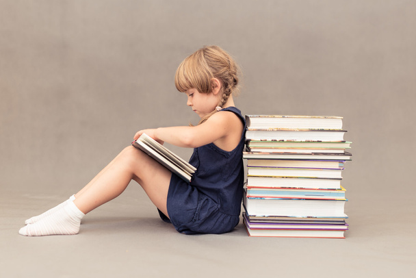 Schoolgirl leaning on a stack of books and reading - Fotó, kép