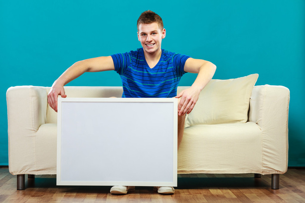 man on sofa holding blank presentation board - Фото, изображение
