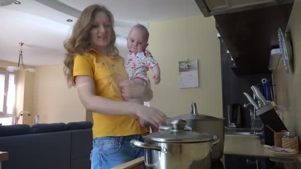 Joven madre sostener bebé niña, preparar la comida en la cocina. 4K
 - Imágenes, Vídeo
