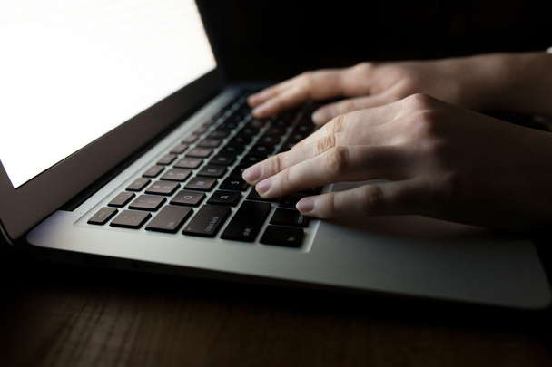 女性の手が、暗闇の中で copyspace のオフィス デスクでノート パソコンを使用して - 写真・画像