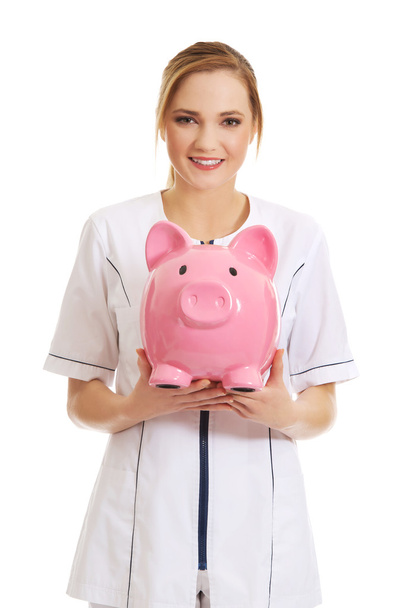Young female doctor holding a piggybank. - Фото, зображення