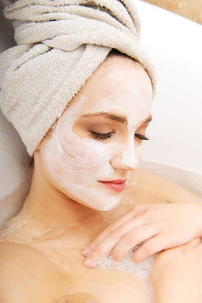 Woman relaxing in bathtub with face mask. - 写真・画像
