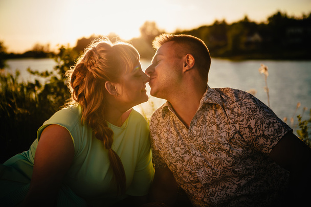 Романтическая пара сидит и целуется на фоне летнего озера
 - Фото, изображение